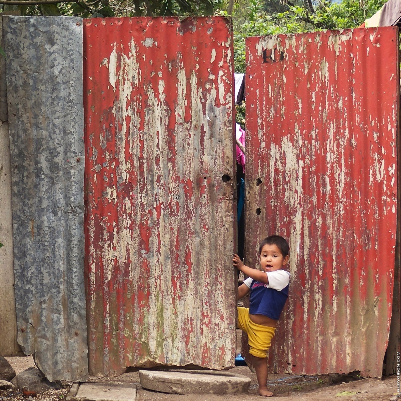Boy opening a red lamina doorway around Antigua Guatemala
