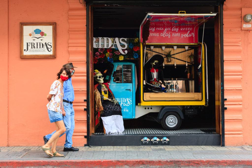 Couple with face masks walks by a Tuk Tuk Bar with Mexican Decoration