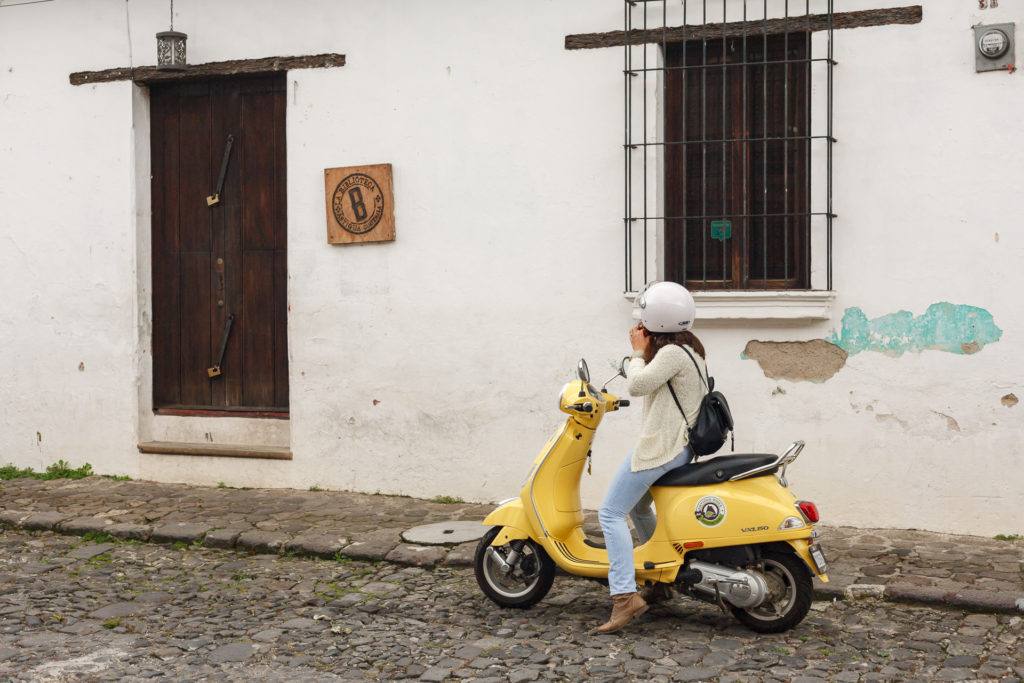 Woman putting on helmet on yellow scooter on the streets of Antigua by RUDY GIRON